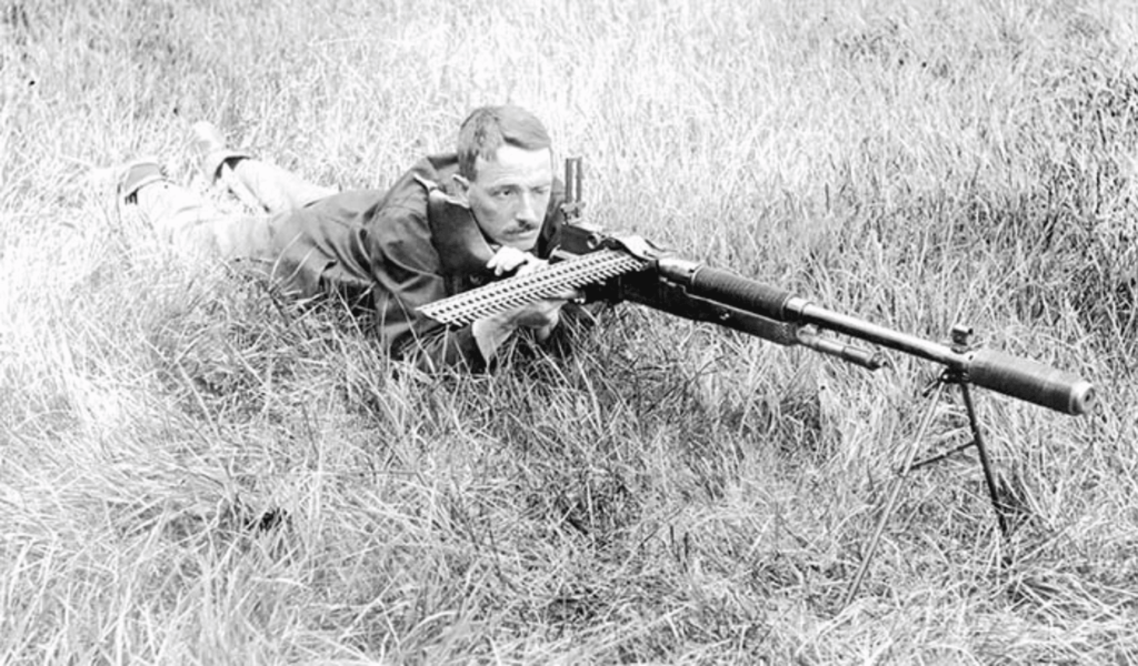 Hiram Percy Maxim laying in grass with suppressed machine gun